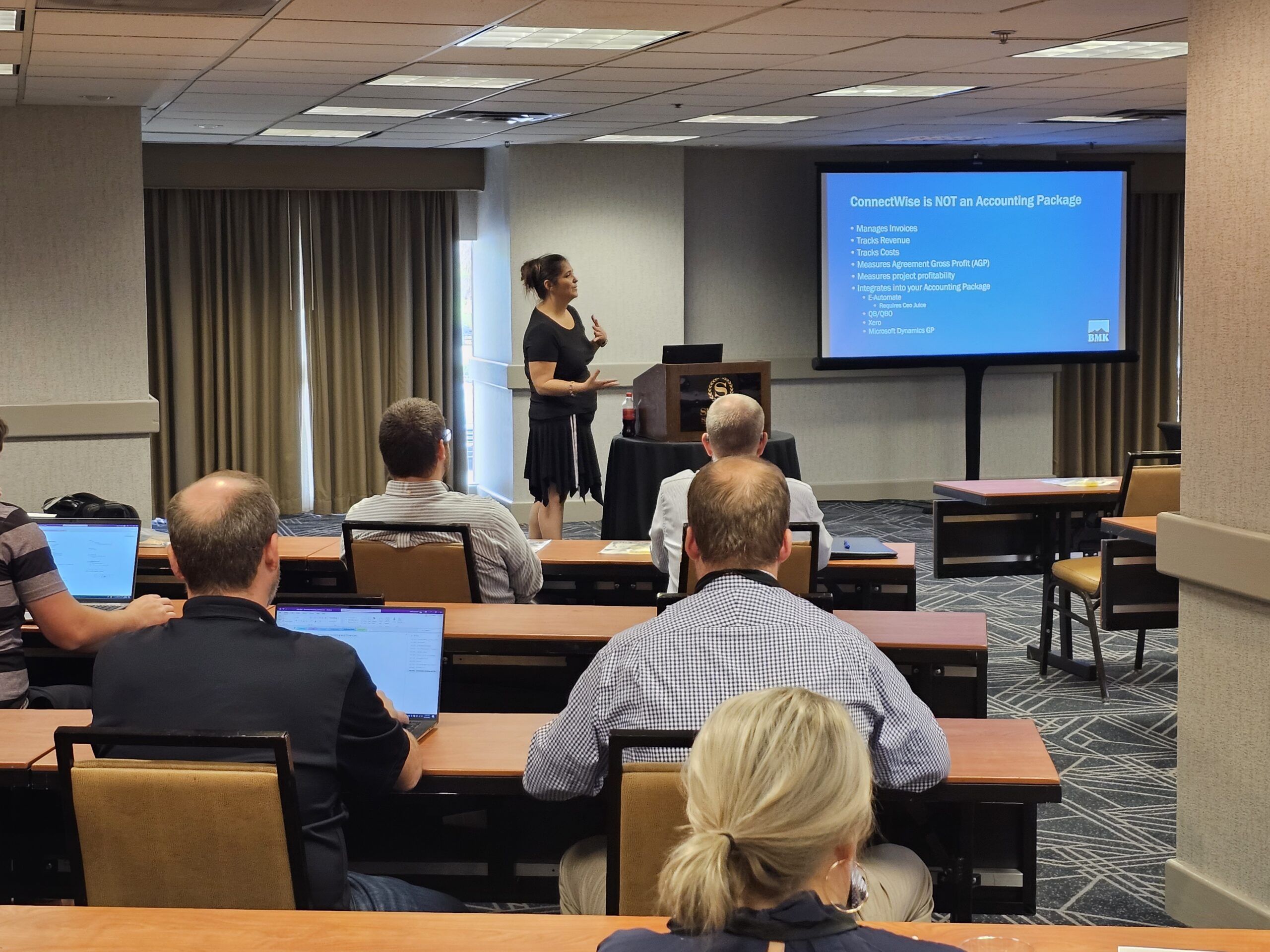 A woman presenting a slide on "ConnectWise is NOT an Accounting Package" to an audience in a conference room with laptops.