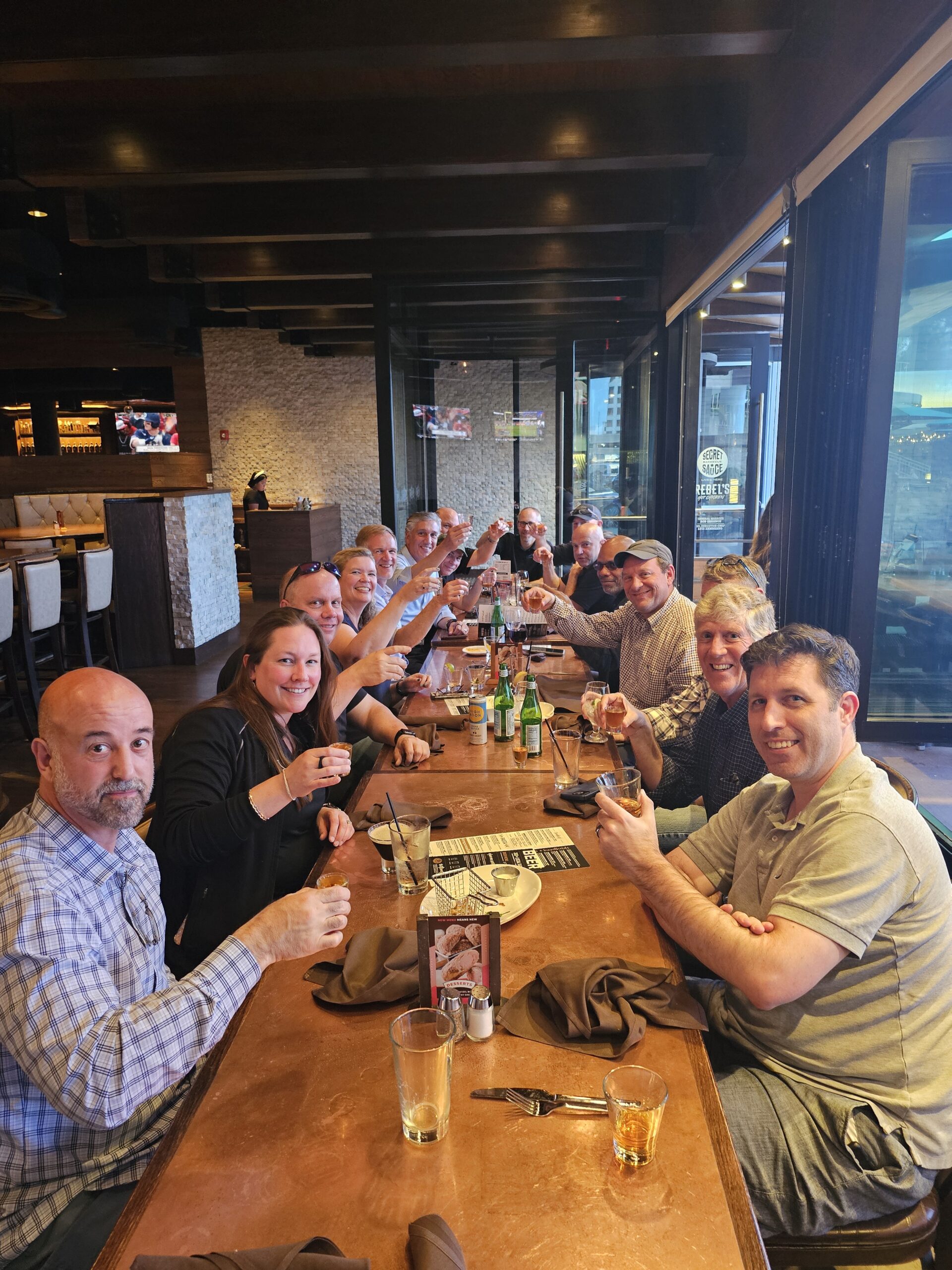A group of people at a restaurant, raising their glasses in a toast, smiling and enjoying a social gathering.